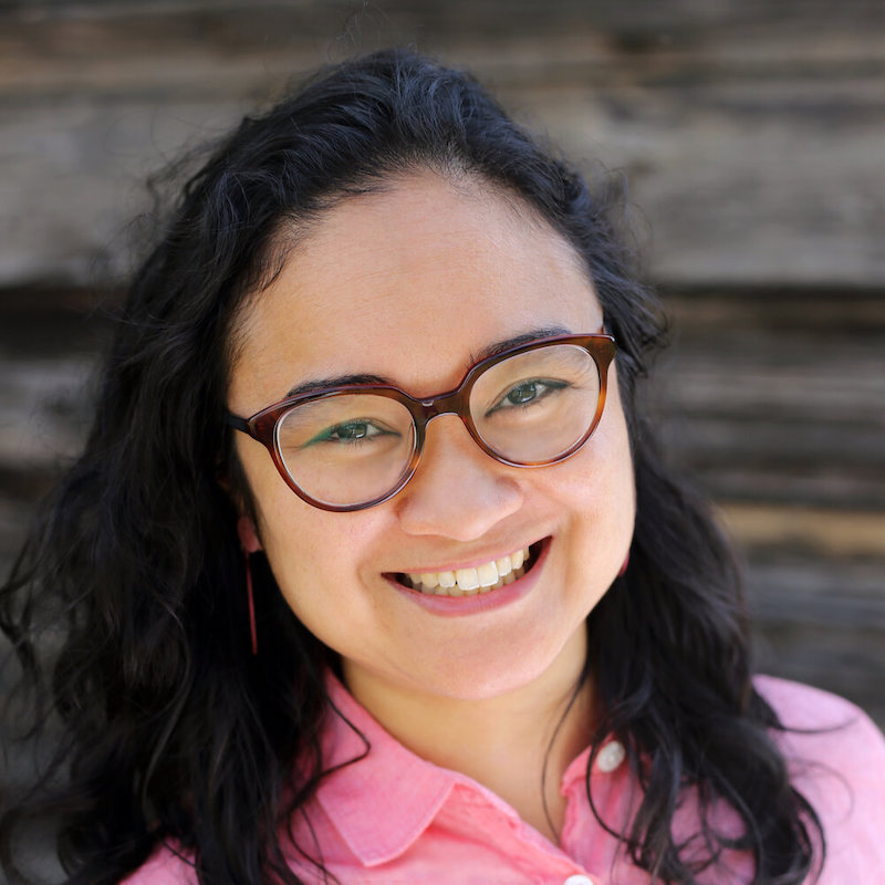 Zhaleh smiling into the camera wearing glasses and a pink shirt