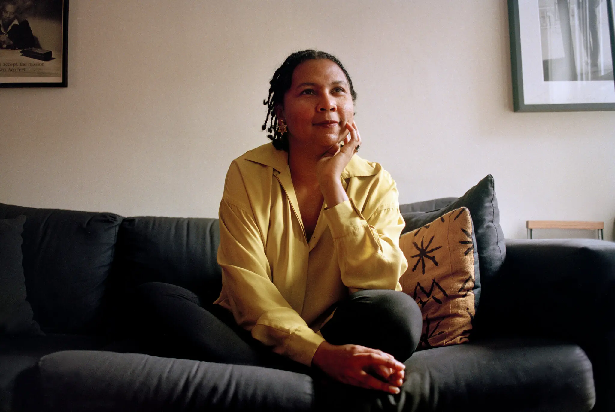 bell hooks sitting on a gray couch, wearing a yellow blouse and gray slacks.