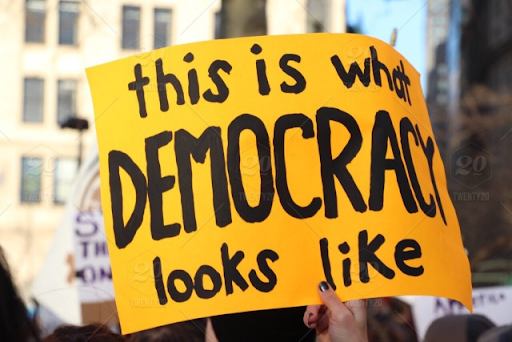Image of a yellow sign with black text reading "This is what DEMOCRACY looks like." 