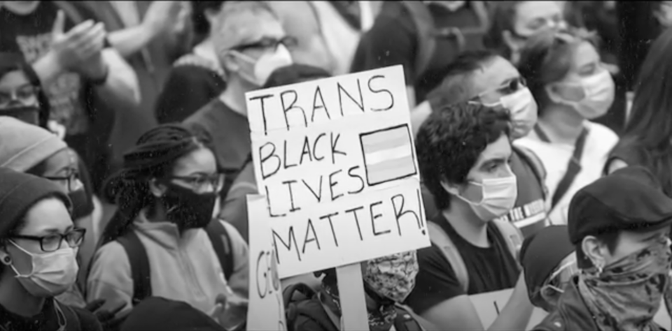 black and white photo of masked protestors. one holds a sign reading "Trans Black Lives Matter."