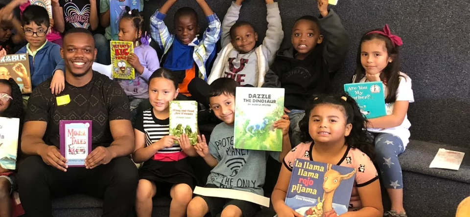 Children smile or raise their hands in celebration while holding a variety of colorful children's books. 