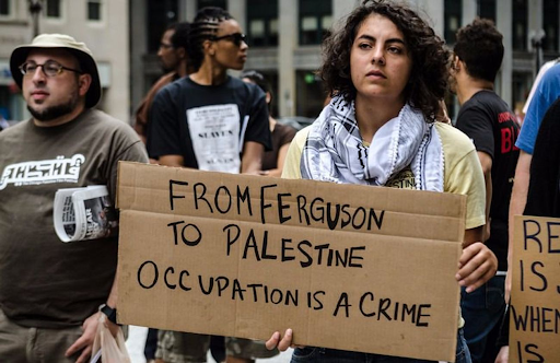 Person at rally holds a sign reading: From Ferguson to Palestine Occupation is a Crime.